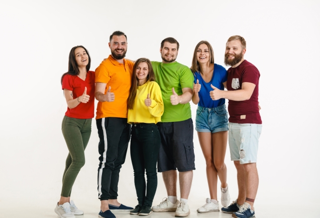 Young man and woman weared in LGBT flag colors on white background. Caucasian models in bright shirts. Look happy, smiling and hugging. LGBT pride, human rights and choice concept.